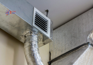 A view of residential HVAC ductwork featuring galvanized metal rectangular ducts, a white louvered air vent, and a flexible silver round duct connected to the main system.