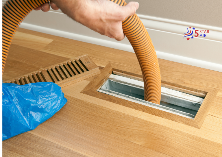 A professional air duct cleaning service using a large orange vacuum hose to remove dust